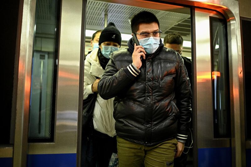 A man wearing a face mask uses his mobile phone as he exits a subway train in Beijing on December 17, 2020. / AFP / NOEL CELIS
