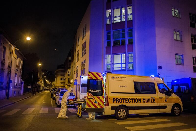 Ambulance crew wheel a trolley bed carrying a patient into an ambulance outside of a residential apartment block in Paris. Bloomberg