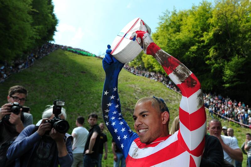 Kenny Rackers from the US celebrates winning the first race down Coopers Hill in pursuit of a fake foam round Double Gloucester cheese during the annual cheese rolling and wake near the village of Brockworth near Gloucester in western England on May 27, 2013. With a disputed history dating back to at least the 1800s, the annual Cooper's Hill Cheese Rolling involves hordes of fearless competitors chasing an eight pound Double Gloucester cheese down a steep hill. The slope has a gradient in places of 1-in-2 and in others 1-in-1, its surface is very rough and uneven and it is almost impossible to remain on foot for the descent. The winner of the race down the hill wins the cheese. AFP PHOTO/CARL COURT
 *** Local Caption ***  209890-01-08.jpg