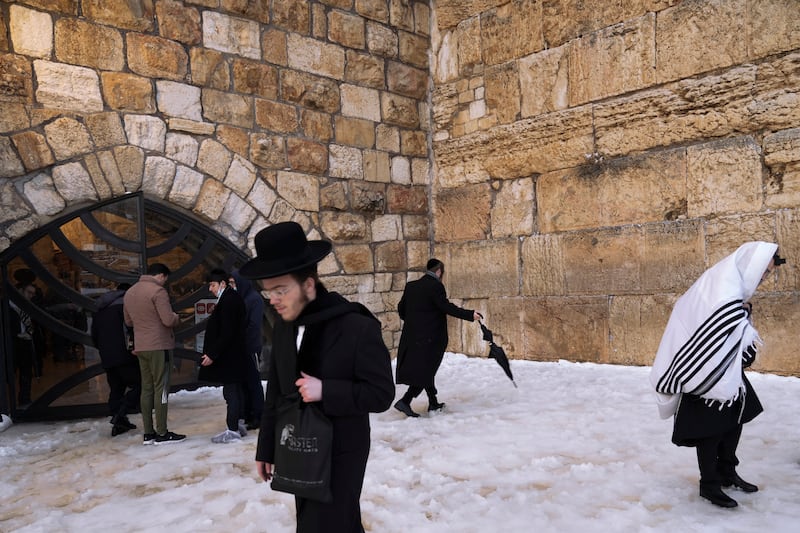 Ultra-Orthodox Jews walk unsteadily on snow-covered ground at the Western Wall. AP