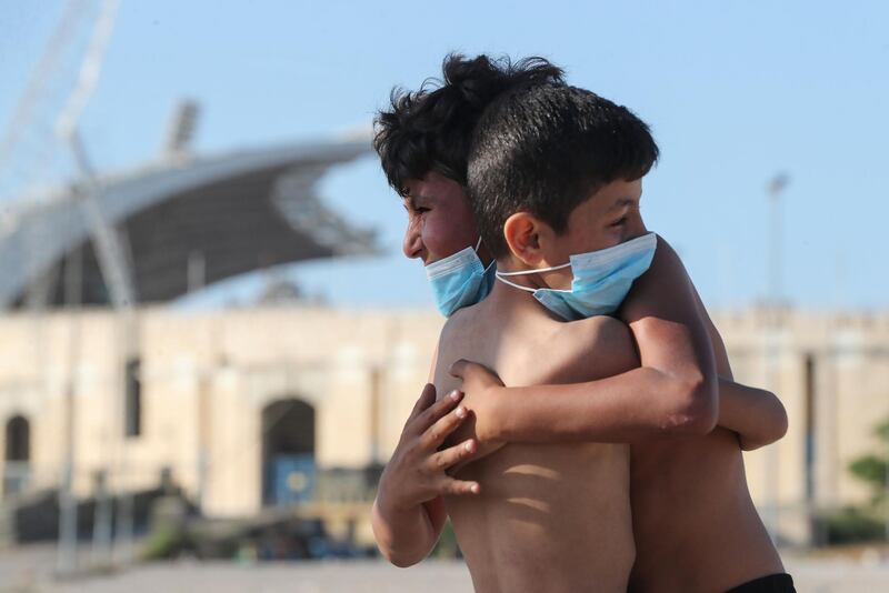 Mask-clad boys hug each other while playing football in front of the Camille Chamoun Sports City Stadium in Beirut.   AFP