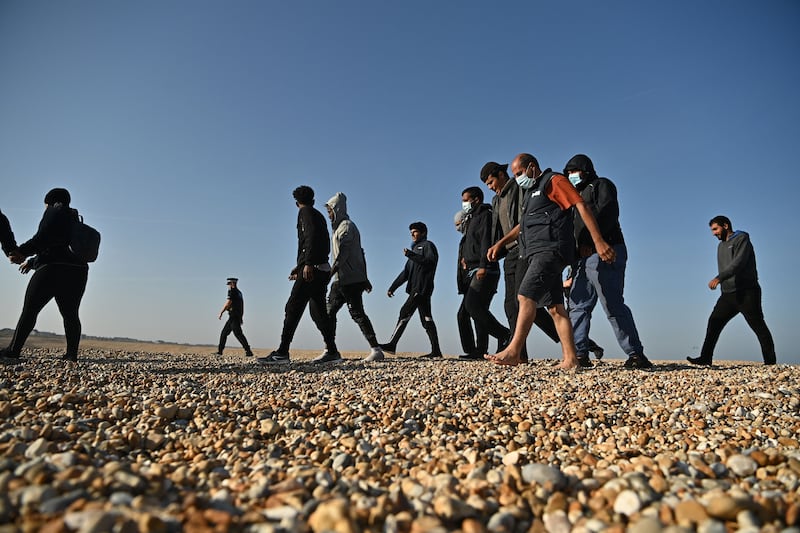 Migrants are escorted across the beach in Dungeness. AFP