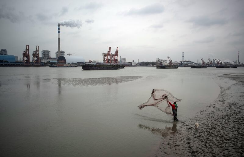 A man catches fish with a net in the Huangpu river across the Wujing Coal-Electricity Power Station in Shanghai on February 21, 2017 / AFP PHOTO / Johannes EISELE
