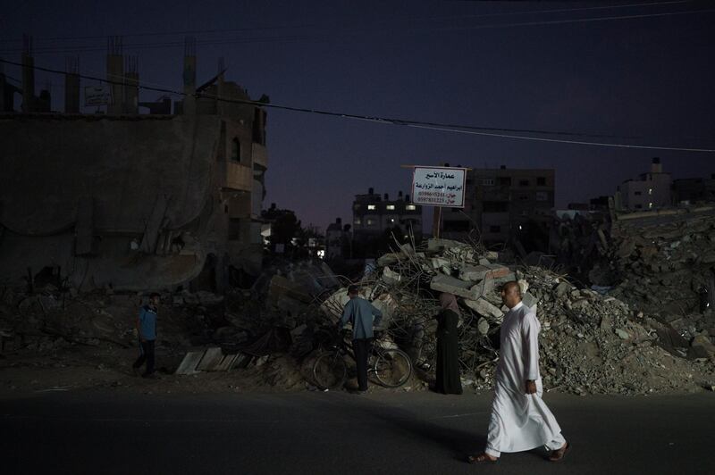 Palestinians walk next to debris of destroyed buildings more than a week after a ceasefire ended an 11-day war between Gaza's Hamas rulers and Israel, in Beit Lahia, northern Gaza Strip. AP Photo