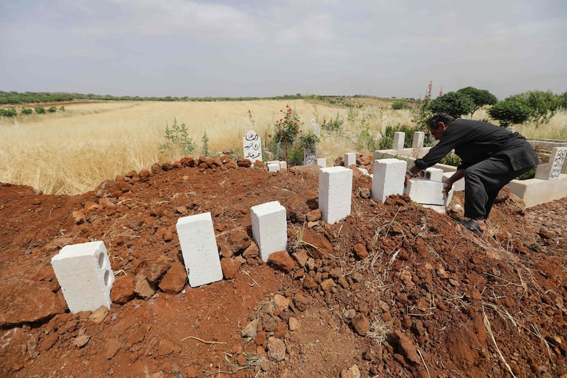 EDITORS NOTE: Graphic content / A Syrian man puts white stones over the tombs of five victims of a regime air strike on the village of Kafr Aweid in which five people, including two children, were killed  following their burial together in the country's northern Idlib province on June 5, 2019. The Idlib region of some three million people has suffered increased regime and Russian air strikes in recent weeks, with hundreds of civilians killed since late April. To keep up, civil defence workers known as the White Helmets are digging graves in advance, to ensure funerals are swift and the few who attend are not killed at the cemetery.
 / AFP / OMAR HAJ KADOUR
