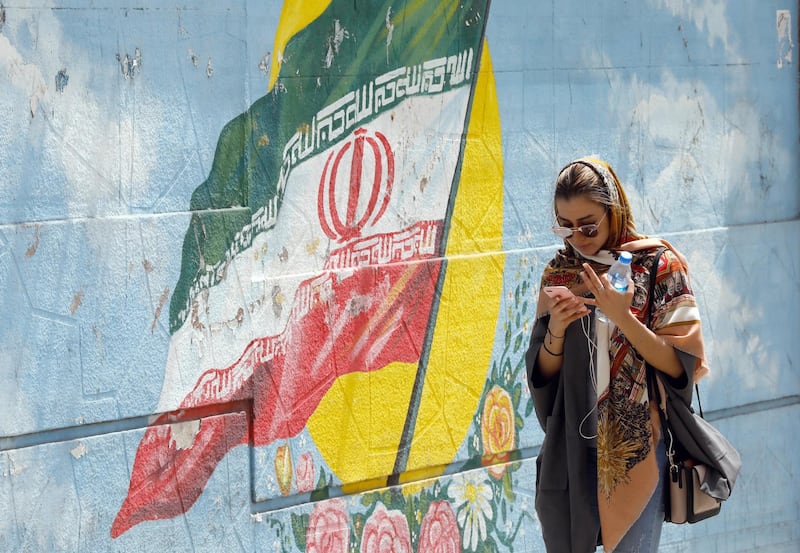 epa06698529 An Iranian girl walks next to a wall painting of Iran's national flag while using her cellphone in a street, in Tehran, Iran, 28 April 2018. Iranian government officially lunched home-made app 'Soroush' with list of emojis in the form of little veiled women with special political messages. The new app was released to replace the popular messaging service Telegram, which was reportedly banned in the county after it was extensively used in communications during the 2017 anti-government protests.  EPA/ABEDIN TAHERKENAREH