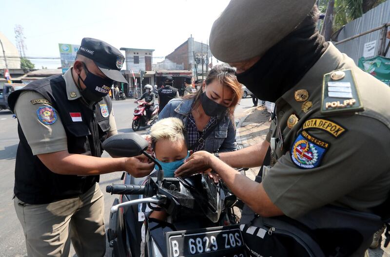 Two Indonesian police officers put a protective face mask on a boy at a checkpoint in Depok, Indonesia.   EPA