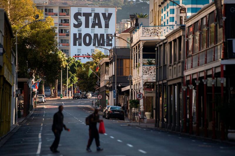 Two men walk across Long Street, usually one of the busiest and most popular entertainment areas with bars, clubs and restaurants in the city, with a billboard reading Stay Home, in Cape Town on April 3, 2020. South Africa came under a nationwide lockdown on March 27, 2020, joining other African countries imposing strict curfews and shutdowns in an attempt to halt the spread of the COVID-19 coronavirus across the continent. / AFP / RODGER BOSCH
