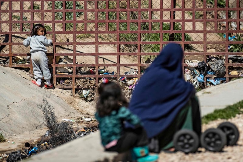 A child plays while a woman sits with another infant on the ground at Camp Roj. AFP