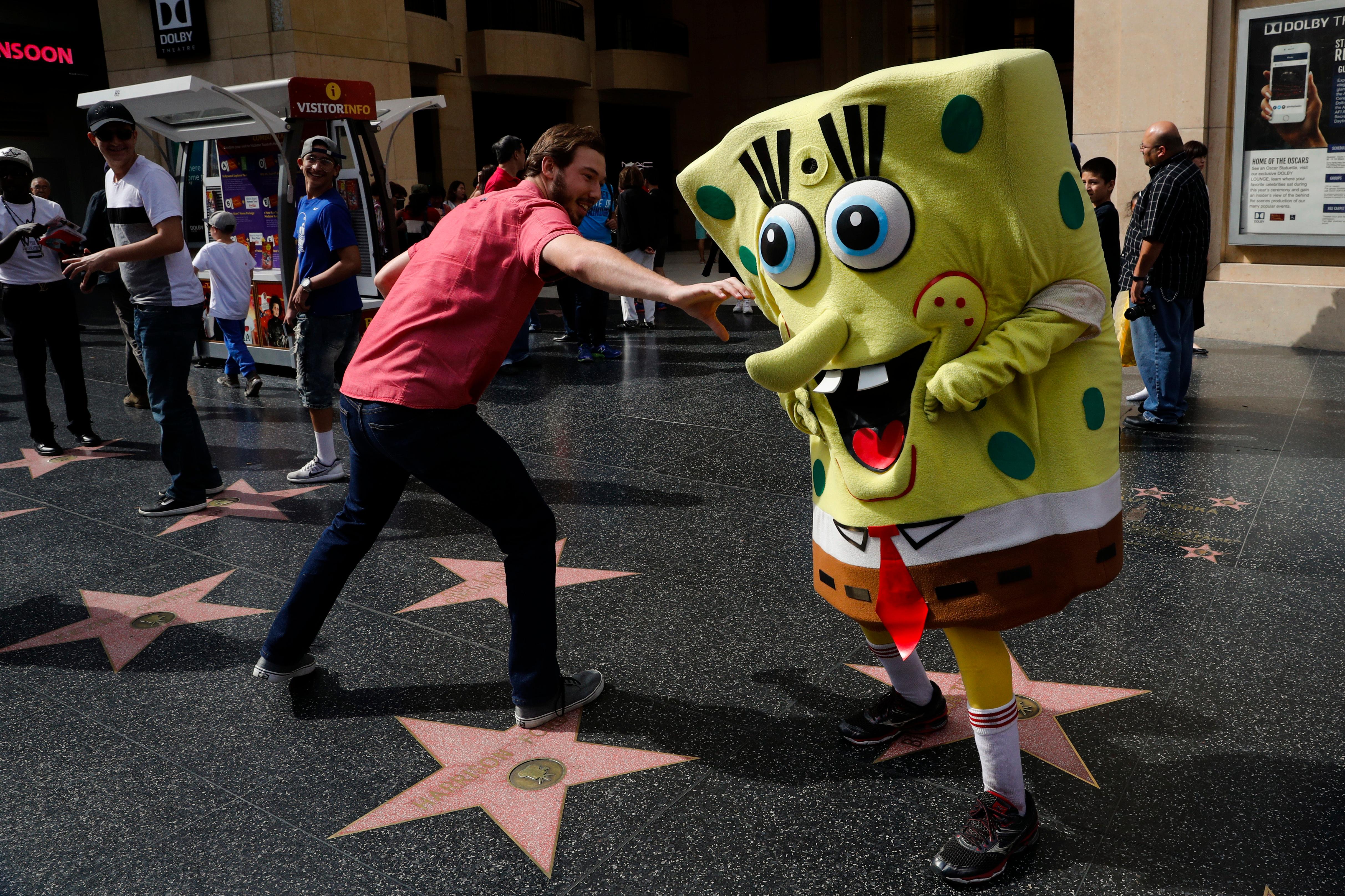 Belnarr Golden, wearing a SpongeBob SquarePants costume, dodges a tourist trying to pull the nose of his costume on Hollywood Boulevard, in Los Angeles. Longtime street performers say the business used to be more lucrative, until the boulevard became overpopulated with costumed characters.  "I crack jokes on them. That's my trick. I make them laugh," said Golden. "If I stand still, I'm not getting paid." Jae C Hong / AP Photo