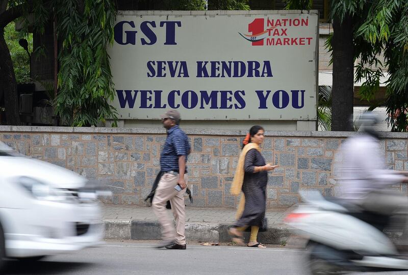 Pedestrians walk in front of a board advertising Goods and Service Tax (GST) in front of the Central Goods and Service Tax office in Bangalore on June 28, 2018.  / AFP / MANJUNATH KIRAN
