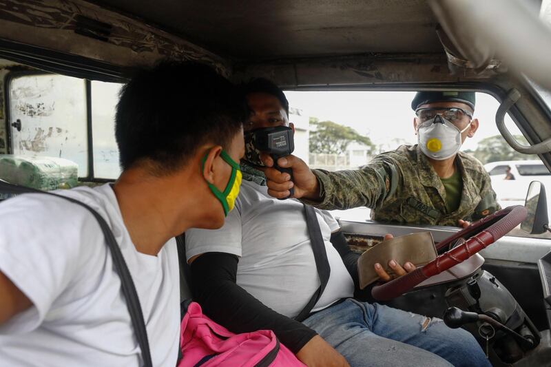 A Philippine Army soldier uses a thermal scanner to check body temperature of two men in a vehicle entering a quarantine border of Quezon City, Metro Manila. EPA