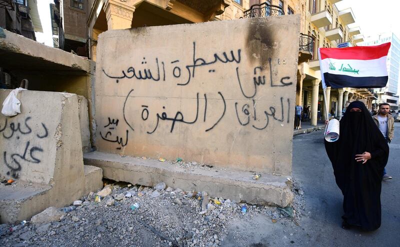 A female protester carrying the Iraqi national flag walks past a concrete block with a slogan reading in Arabic: 'The checkpoint of the people, long live Iraq' written on it, during a protest at the Tahrir square in central Baghdad. EPA