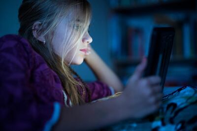 Beautiful long haired teenager girl reading from tablet, in the dark room at night in the bed, with her face illuminated by the screen. Getty Images