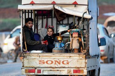 A young man and a girl sit in the back of a truck loaded with a motorcycle, waterpipe, and gas cylinder, passing by an internally-displaced persons (IDP) camp by Dayr Ballut near the Turkish border in the west of Syria's northern province of Aleppo on February 16, 2020, as people flee advancing Syrian government forces in Idlib and Aleppo provinces.  AFP