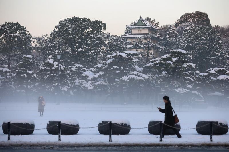 A man walks past as a woman takes photographs on the snow-covered grounds of the Imperial Palace in Tokyo on Tuesday. Takaaki Iwabu / Bloomberg
