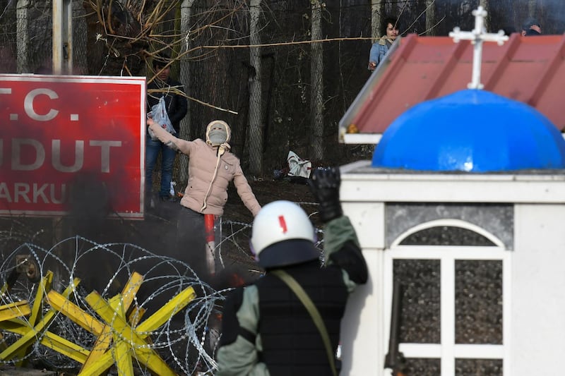 A hooded migrant who, along with other migrants wants to cross into Greece from Turkey's Pazarkule border crossing, prepares to throw a stone at a Greek riot police officer, in Kastanies, Greece. REUTERS