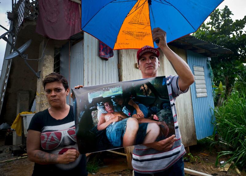 Blanca Rivera and Eduard Rodriguez pose with a printed photo of them that was taken on September 30, 2017 of them sleeping in their car. The couple said authorities rejected their request for financial help to rebuild, so they sold their car to build a room next to his mother's house.