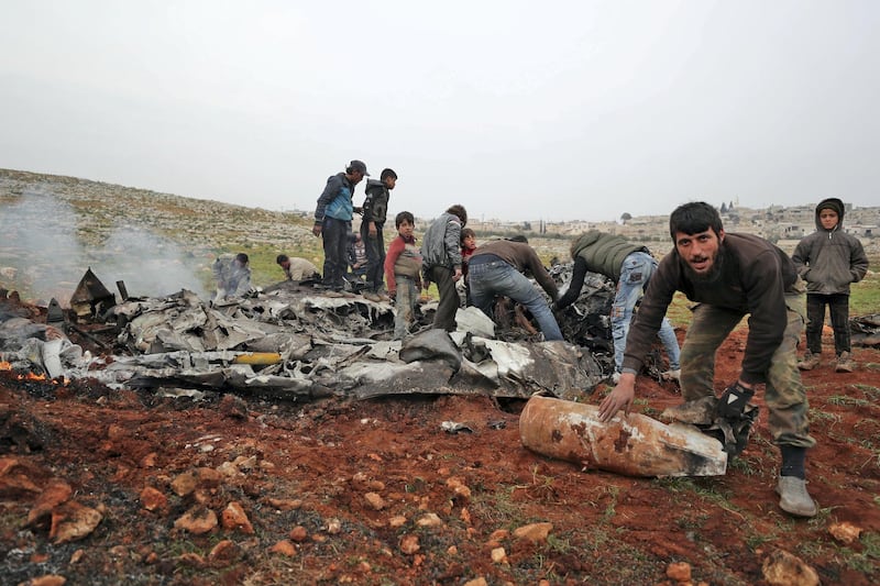 People search for scraps of metal among the debris of a Syrian military helicopter that was shot down on February 14, 2020, in the western countryside of Aleppo province. - The  helicopter was shot down over the last major rebel bastion in northwest Syria, killing two pilots, a war monitor said, in the second such incident this week. (Photo by Omar HAJ KADOUR / AFP)