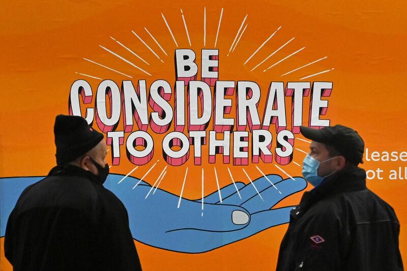 Travellers stand on a London Underground platform with a sign urging people to be considerate to others in London. AFP