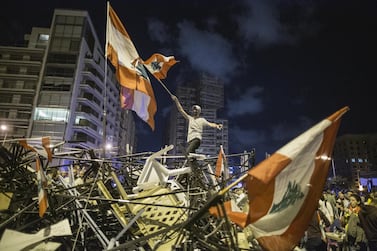 An anti-government protester waves a Lebanese flag as he stands on top of a pile of broken tents in Martyrs' Square in Beirut. Getty