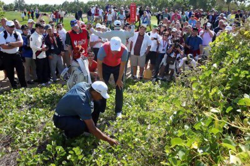 Tiger Woods, left, checks the lie of his golf ball, assisted by Martin Kaymer on the 5th hole during the second round of the Abu Dhabi HSBC Golf Championship on Friday. Woods, along with world No 1 Rory McIlroy, missed the cut.