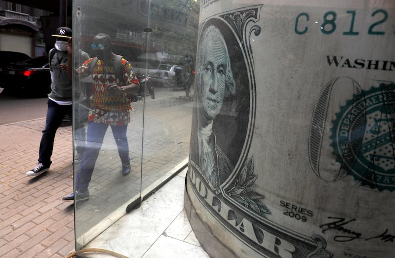 A man wears a protective mask following an outbreak of the coronavirus and walks with his friend in front of a currency exchange bureau advertisement showing an image of the U.S. dollar in the Egyptian capital Cairo. Reuters