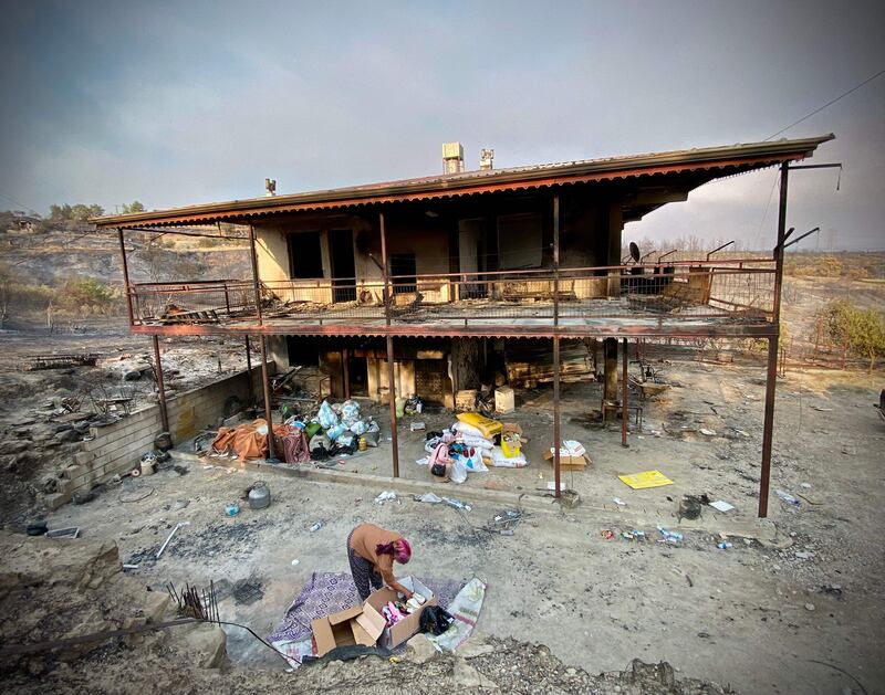 A woman puts away belongings in front of a burnt house, near Manavgat.