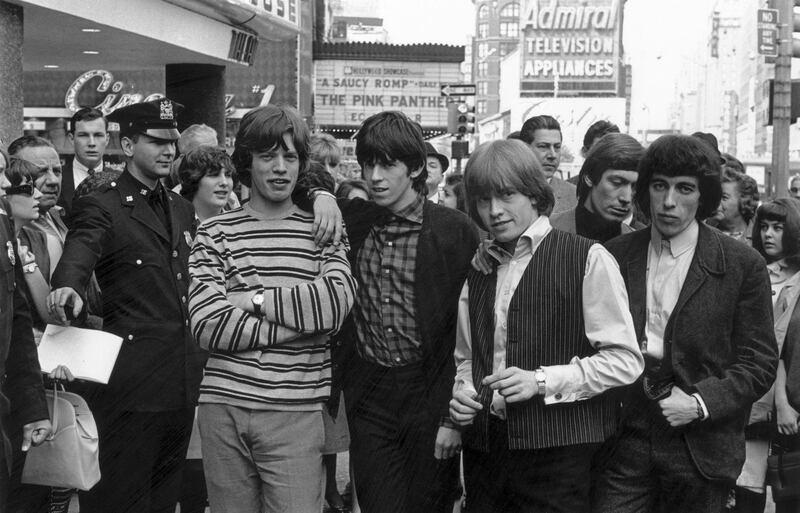 June 1964:  From left to right; Mick Jagger, Keith Richards, Brian Jones  (1942 - 1969), Charlie Watts and Bill Wyman of the Rolling Stones pose for a photo in a New York street, while a policeman holds back some curious spectators.  (Photo by William Lovelace/Express/Getty Images)