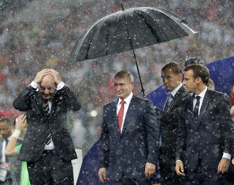 FIFA President Gianni Infantino, left, gestures as Russian President Vladimir Putin stands underneath an umbrella watched by French President Emmanuel Macron after the final match between France and Croatia at the 2018 soccer World Cup in the Luzhniki Stadium in Moscow, Russia, Sunday, July 15, 2018. France won the final 4-2. (AP Photo/Matthias Schrader)