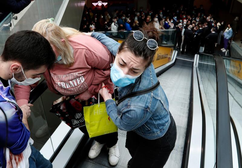 An elderly woman is helped up an escalator as people queue to get vaccinated and be one of 100 people to receive shopping coupons, along with the jabs,  in the Usce shopping mall in Belgrade, Serbia. AP Photo