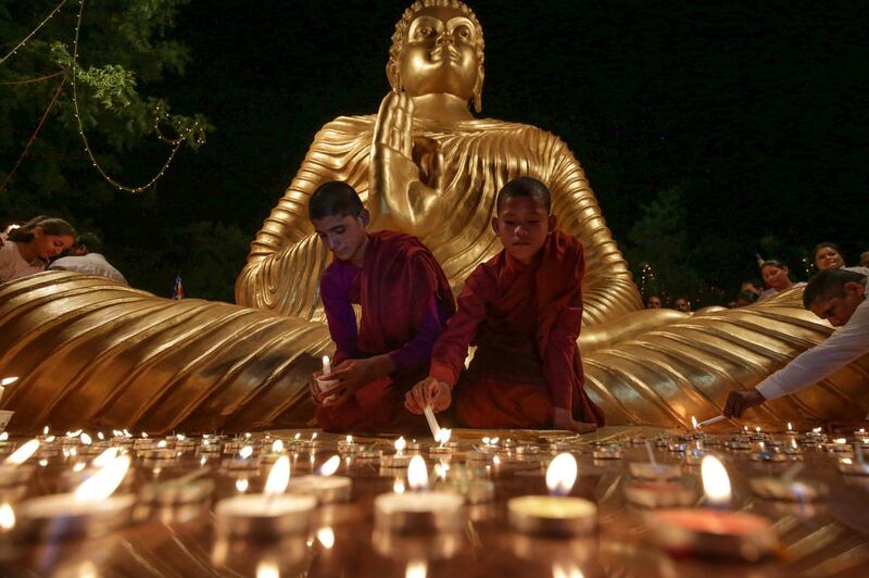 Young Buddhist monks light candles at the bottom of a giant statue of Buddha on the eve of Vesak Day, in Bhopal, India.  AFP