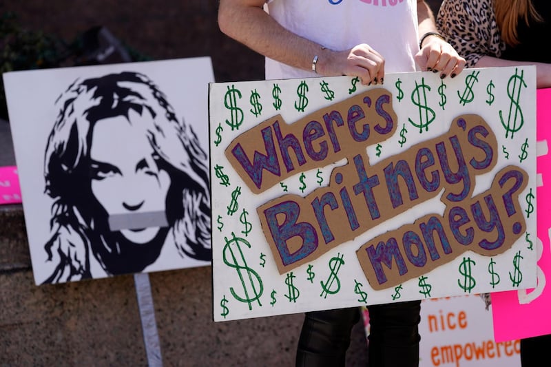 A Britney Spears supporter holds a sign near a portrait of her outside a court hearing concerning the pop singer's conservatorship at the Stanley Mosk Courthouse, Wednesday, March 17, 2021, in Los Angeles. Attorneys for Spears and lawyers for her father Jamie Spears jointly asked the judge to delay an accounting and status report on the conservatorship until April 27. (AP Photo/Chris Pizzello)