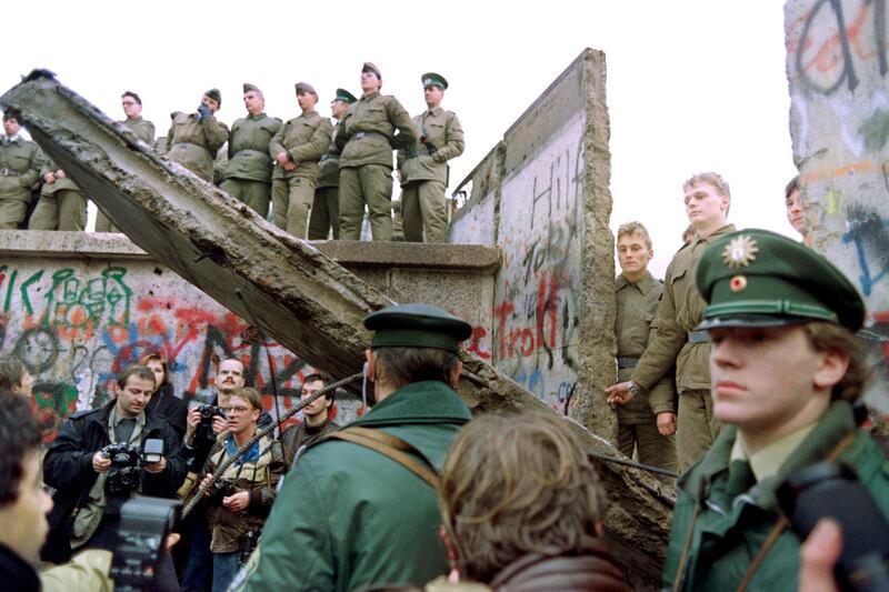 Two West German policemen prevent people from approaching as East German Vopos stand on and near a fallen portion of the Berlin Wall 11 November 1989. Two days before, Gunter Schabowski, the East Berlin Communist party boss, declared that starting from midnight, East Germans would be free to leave the country, without permission, at any point along the border, including the crossing-points through the Wall in Berlin. The Berlin concrete wall was built by the East German government in August 1961 to seal off East Berlin from the part of the city occupied by the three main Western powers to prevent mass illegal immigration to the West. According to the "August 13 Association" which specialises in the history of the Berlin Wall, at least 938 people - 255 in Berlin alone - died, shot by East German border guards, attempting to flee to West Berlin or West Germany. AFP PHOTO GERERAD MALIE (Photo by GERARD MALIE / AFP)