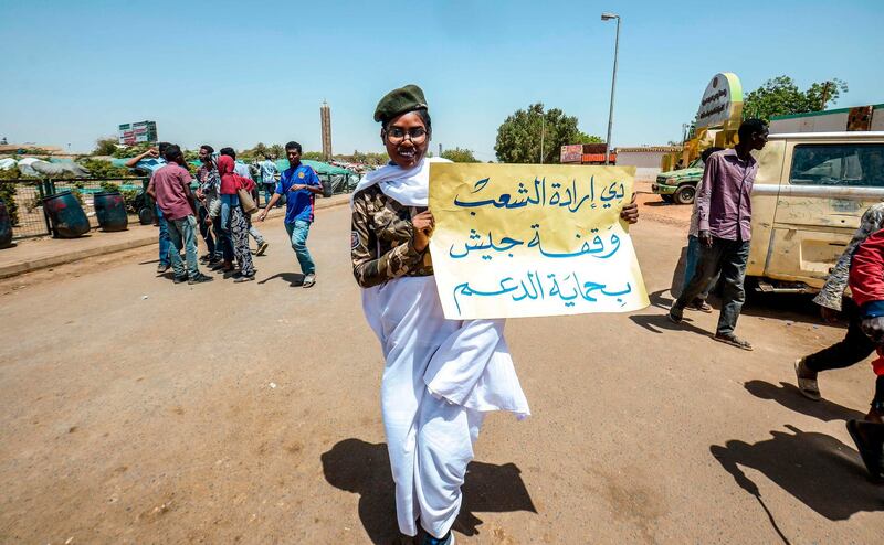 A Sudanese woman dressed in a white garb surrounding clothes coloured with camouflage patters and wearing a green beret holds up a sign reading in vernacular Arabic "this is the will of the people, an Army stand supported by the [Rapid] Support [Forces]".  AFP