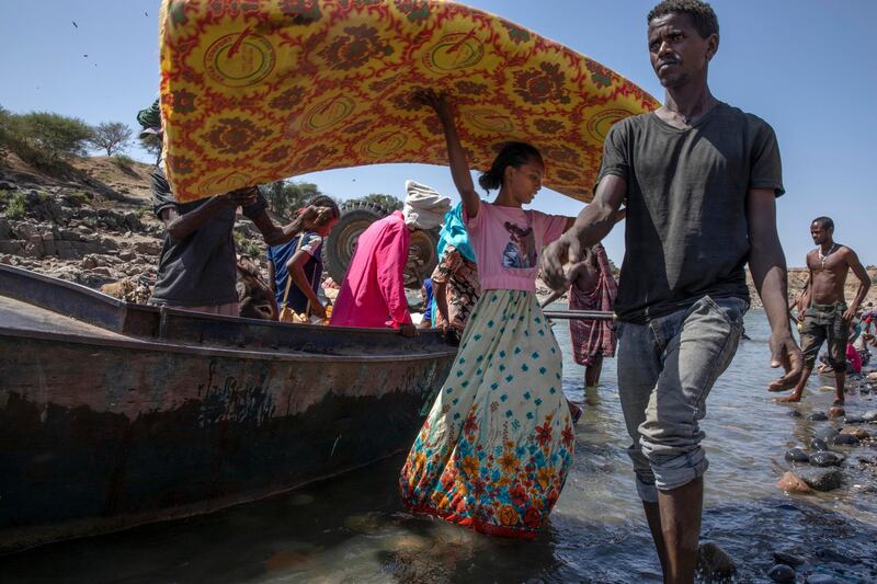 Refugees who fled the conflict in Ethiopia's Tigray region carry their belongings off a boat after arriving on the banks of the Tekeze River on the Sudan-Ethiopia border. AP