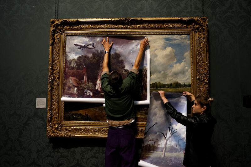 Activists from the 'Just Stop Oil' campaign group cover 'The Hay Wain' painting by English artist John Constable, in a mock 'undated' version including roads and aircraft, before glueing their hands to the frame in protest against the use of fossil fuels, at The National Gallery in London on July 4. AFP
