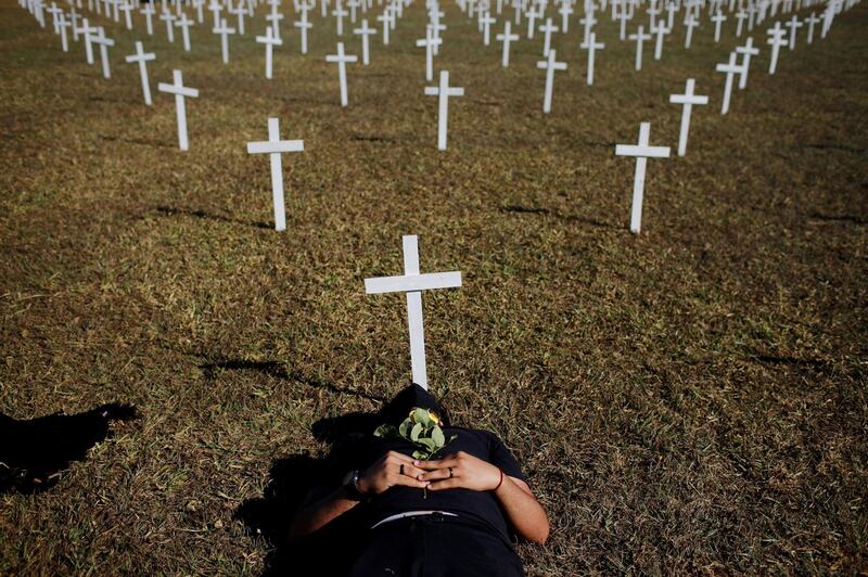 An activist lies next to crosses symbolising those who died from the coronavirus in front of the National Congress during a protest against Brazil's President Jair Bolsonaro in Brasilia. Reuters