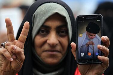 A demonstrator in Baghdad shows an image of Moqtada Al Sadr on her phone. Impoverished members of the Shiite community living in the Iraqi capital and the south of the country comprise the core of Mr Al Sadr's support. AFP 