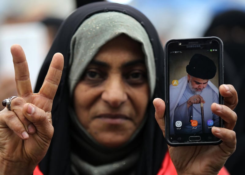 An Iraqi woman flashes the victory sign and displays an image of Iraqi Shiite cleric Moqtada al-Sadr on her phone, as she takes part in a demonstration on al-Jumhuriya bridge in the capital Baghdad on December 13, 2019, amid ongoing anti-government protests. Iraq's capital and Shiite-majority south have been gripped Since October 1, by rallies against corruption, poor public services, a lack of jobs and Iran's perceived political interference. / AFP / AHMAD AL-RUBAYE
