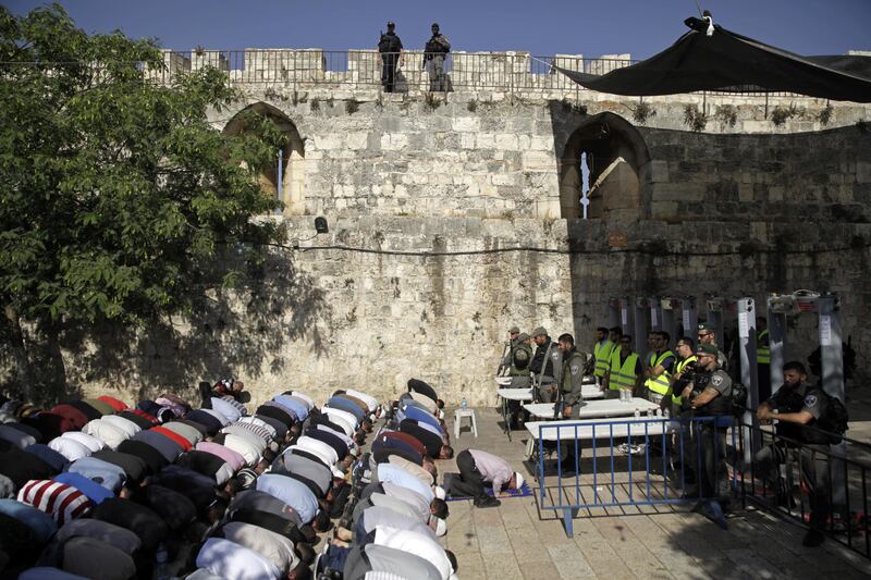 Israeli border police officers stand guard as Muslim men pray outside the Al Aqsa Mosque compound, in Jerusalem, Sunday, July 16, 2017. Adnan Husseini, the Palestinian Minister of Jerusalem, said Sunday that arrangements at the Muslim-administered holy site need to return to how they were before a deadly attack last week, in which three Arab Israelis shot dead two police officers before being killed. (AP Photo/Mahmoud Illean)