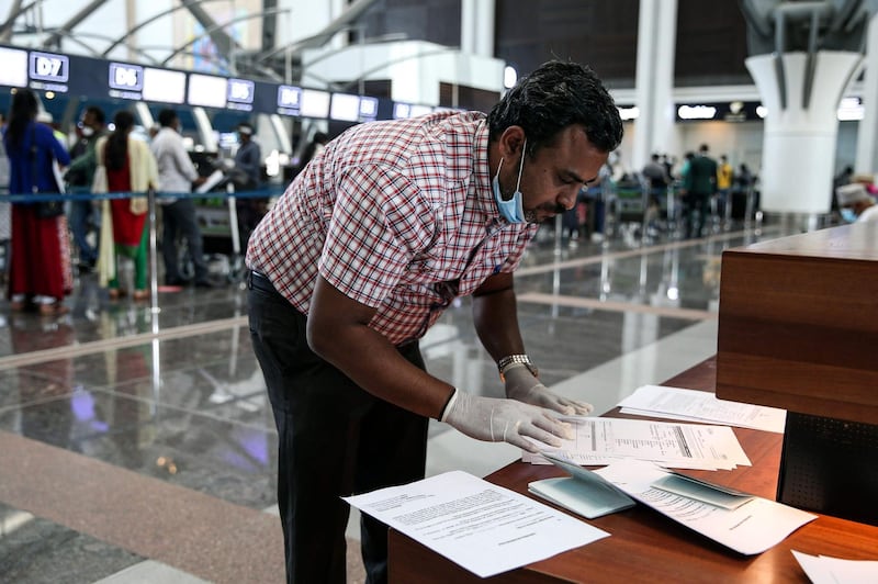 A man wearing latex gloves and a mask, due to the coronavirus pandemic, checks airline tickets and travel documents while behind him Indian nationals residing in Oman queue with their luggage in Muscat International Airport ahead of their repatriation flight from the Omani capital, on May 12, 2020.  AFP