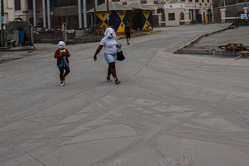 A woman and child cover their heads and faces as they walk across a road in Kingstown strewn with fine ash. AP Photo