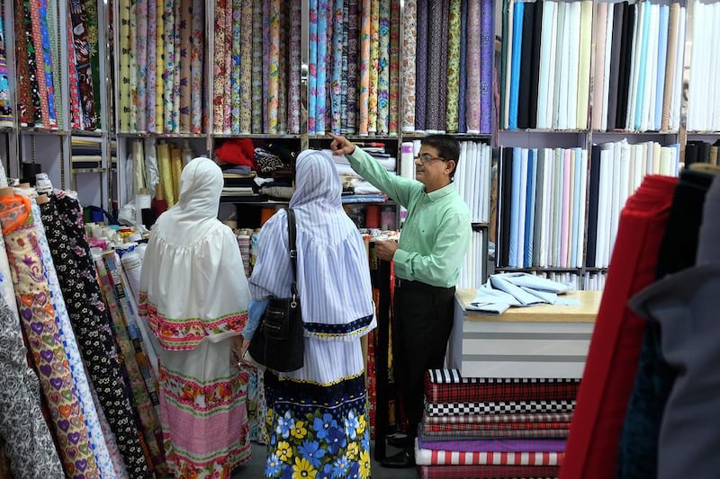 Narendra Devnani helps his customers pick up the right fabric at his textile shop, Champion Textiles, in Satwa in Dubai. Delores Johnson / The National  