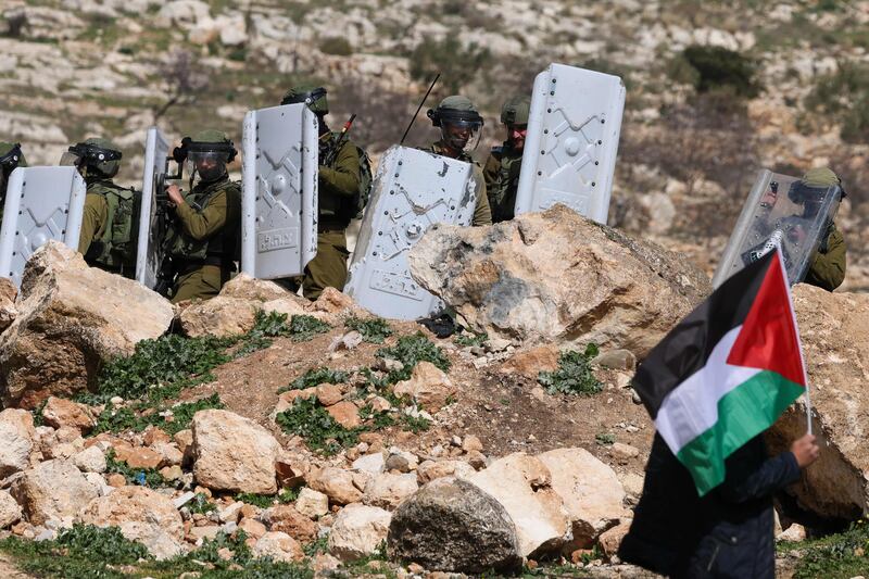 A Palestinian protester waves a flag near the Israeli security forces during a demonstration against the Israeli outposts in the occupied West Bank city of Nablus. AFP
