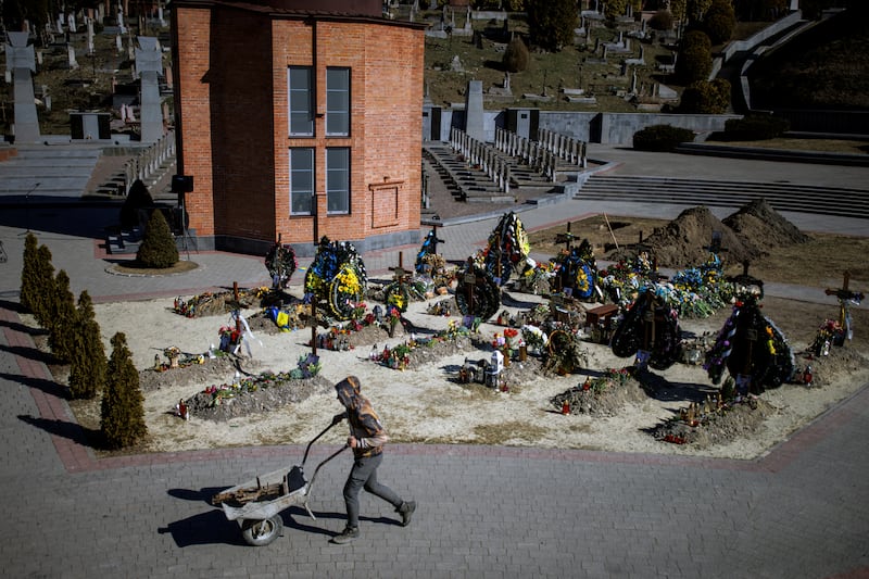 A worker pushes a cart past graves of Ukrainian soldiers who were killed in battle during Russia’s attack on Ukraine, at the Lychakiv cemetery in Lviv. Reuters