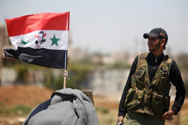 A Syrian army soldier stands next to a Syrian flag in Umm al-Mayazen, in the countryside of Deraa, Syria, July 10, 2018. REUTERS/Omar Sanadiki