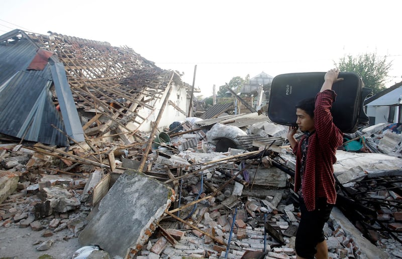 A man carries his belongings past the ruin of houses at a village affected by an earthquake in North Lombok, Indonesia. AP Photo
