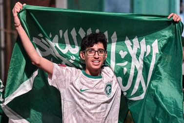 A Saudi football fan poses with his country's flag during celebrations of Saudi Arabia's win over Argentina in the Qatar 2022 World Cup in the capital Riyadh on November 22, 2022.  - Disbelieving Saudis formed impromptu dance circles and waved the sword-emblazoned national flag from the windows of speeding cars in Riyadh on November 22 after their team's sensational win over Lionel Messi's Argentina.  As the final whistle blew in the group-stage shocker with a 2-1 scorecard that ended Argentina's 36-match unbeaten streak, fans watching on a big screen at a stadium in the capital Riyadh sent shisha pipes flying as they rushed to celebrate.  (Photo by AFP)