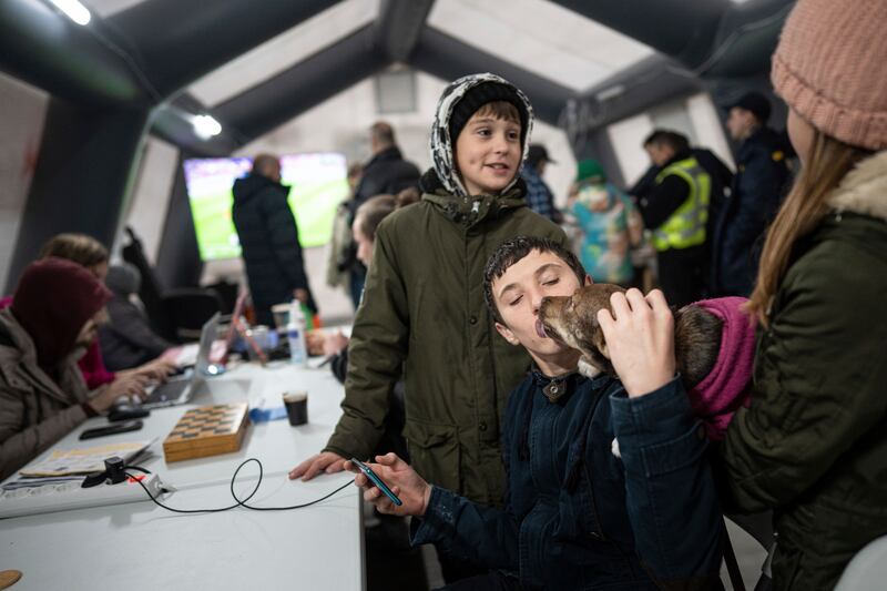 A boy kisses a dog while he charges his phone at the heating tent dubbed a Point of Invincibly in Bucha, Ukraine. AP